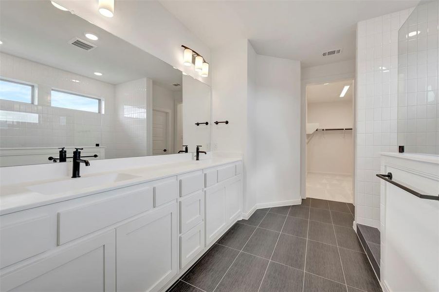 Full bath with a spacious closet, double vanity, dark tile patterned flooring, walk in shower, and recessed lighting