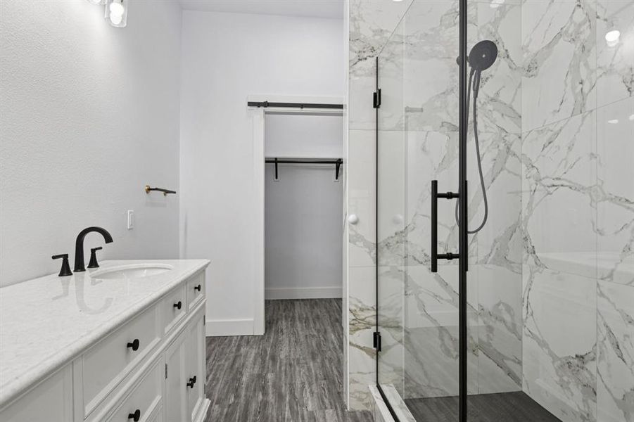 Full bath featuring vanity, a marble finish shower, dark wood-style floors, and a spacious closet Full bath featuring vanity, a marble finish shower, dark wood-style floors, and a spacious closet