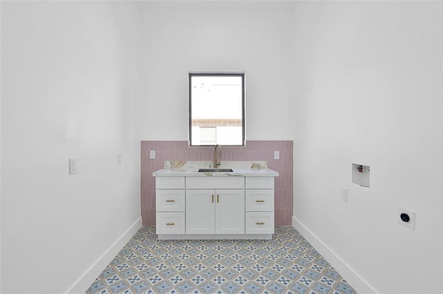 Spacious laundry room featuring electric and gas dryer hookups, a convenient sink, and elegant porcelain tile accents.