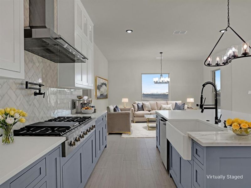 Kitchen with wall chimney exhaust hood, light stone counters, hanging light fixtures, appliances with stainless steel finishes, and gray cabinets