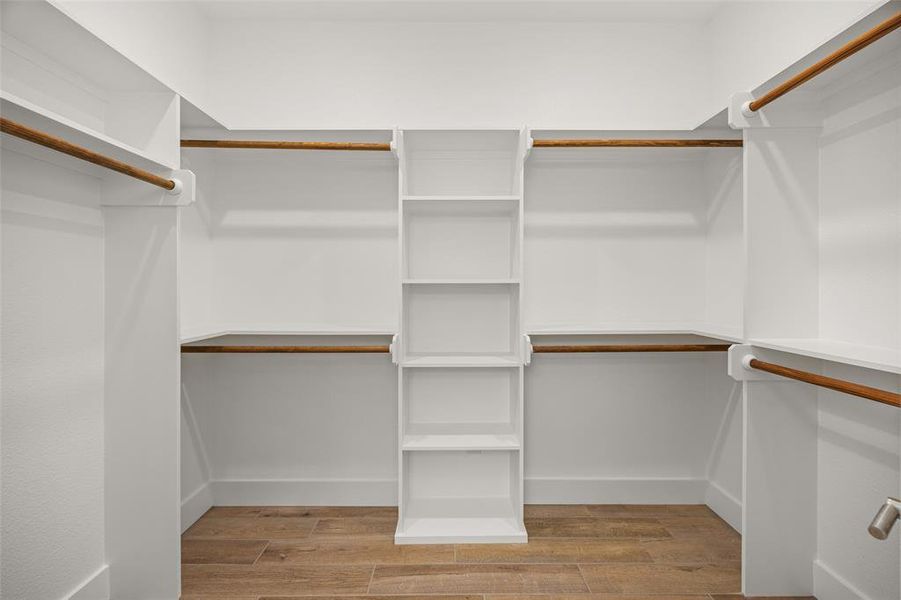 Walk-in closet featuring white built-in shelving, multiple hanging rods, and wood-finish flooring