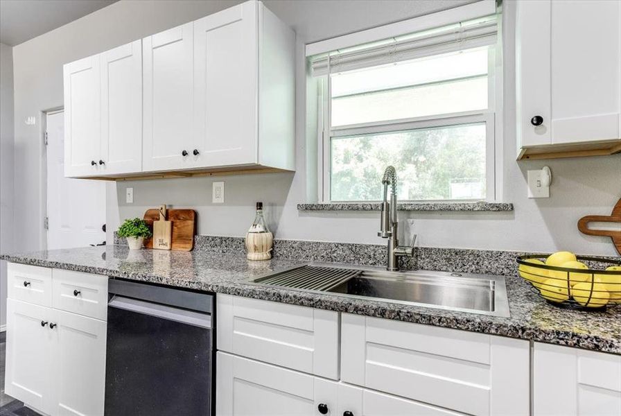 Kitchen featuring white shaker-style cabinetry, dark speckled countertops, and a stainless steel undermount sink with a gooseneck faucet