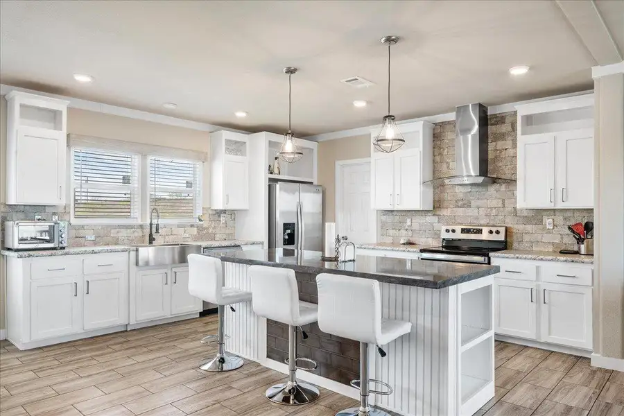 Kitchen with tasteful backsplash, a kitchen island with sink, white cabinets, and stainless steel appliances Kitchen with tasteful backsplash, a kitchen island with sink, white cabinets, and stainless steel appliances