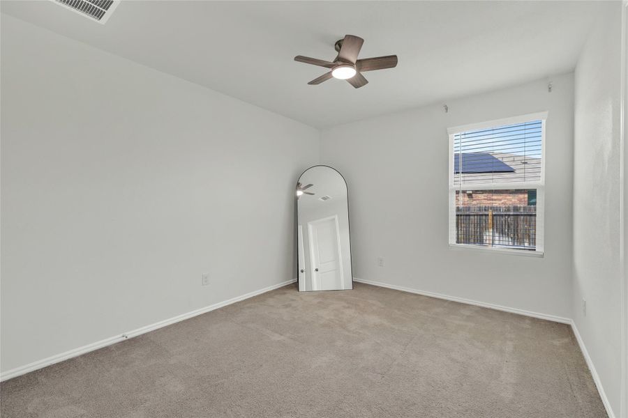A well-lit bedroom with soft carpeting and a contemporary ceiling fan, ready for personal touches.