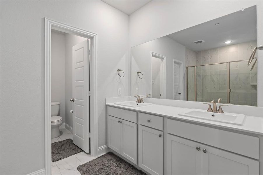 Bathroom featuring tile patterned floors, double sink vanity, walk in shower, and toilet