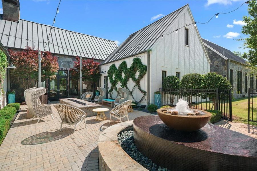 Expansive brick paver patio featuring a built-in fire pit, a tiered water feature, and string lighting