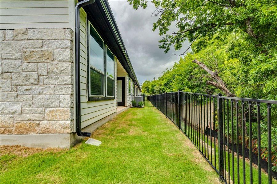 A well-maintained side yard with a sturdy metal fence bordering lush green trees.
