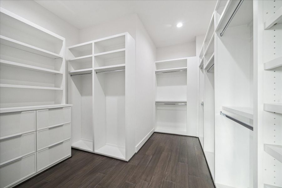 Custom-designed walk-in closet with extensive built-in shelving, hanging space, and integrated drawer storage. Thoughtfully configured layout maximizes organization while maintaining a bright, clean aesthetic. Wide-plank flooring and recessed lighting continue the home’s consistent, upscale finish throughout.