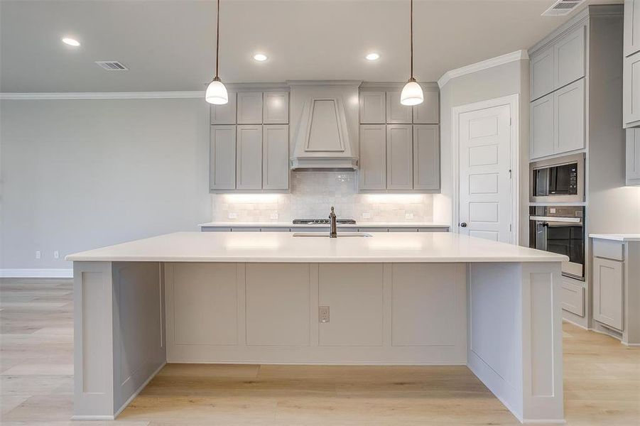 Kitchen with custom range hood, light hardwood / wood-style flooring, a kitchen island with sink, gray cabinets, and oven