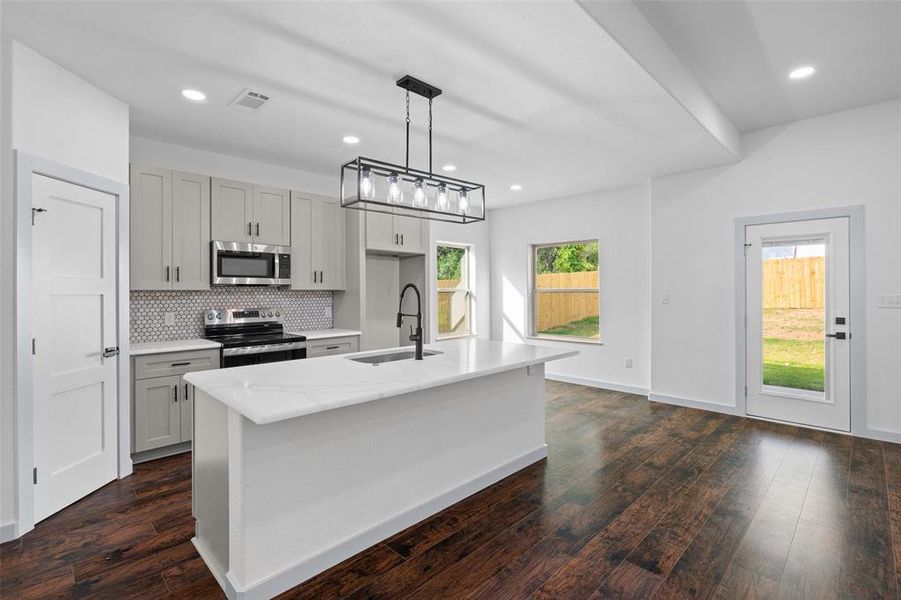 Kitchen featuring healthy amount of natural light, tasteful backsplash, stainless steel appliances, light stone counters, and recessed lighting
