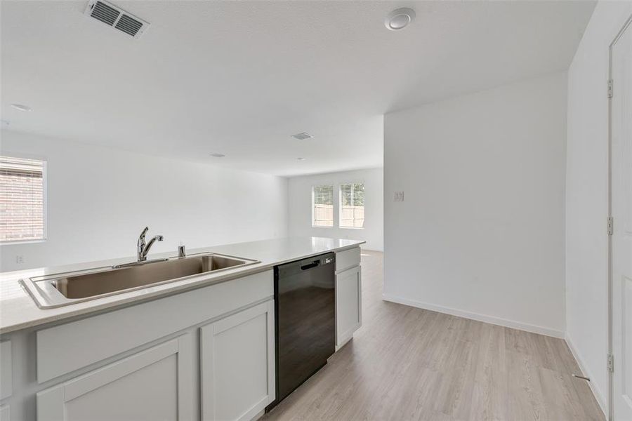 Kitchen featuring white cabinetry, sink, light wood-type flooring, and black dishwasher