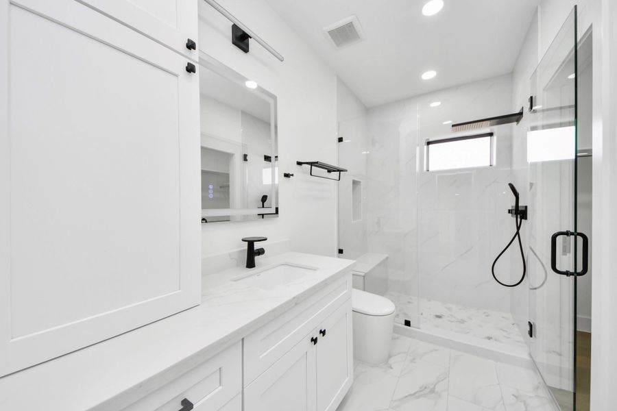 The secondary bathroom boasts a large standing shower and ample cabinetry, providing both practicality and a polished, high-end aesthetic.