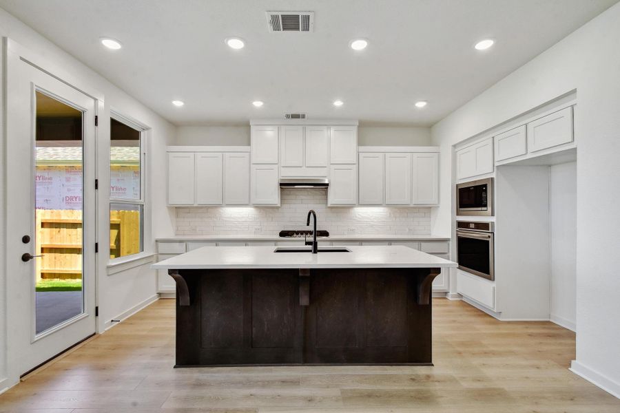 Kitchen with stainless steel appliances, an island with sink, backsplash, light countertops, and recessed lighting