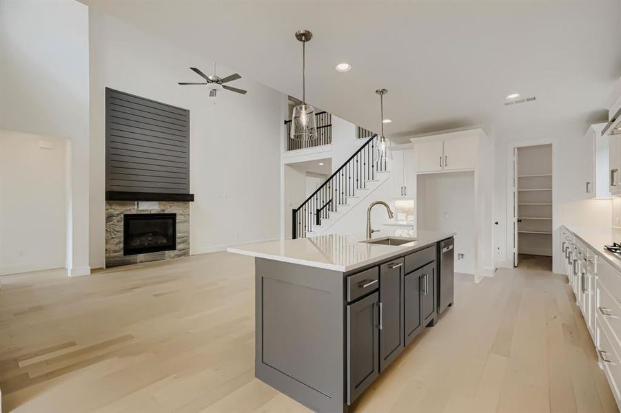 Dual tone kitchen with two tone cabinets, a kitchen island with sink, light wood-style floors, a tile fireplace, and open floor plan