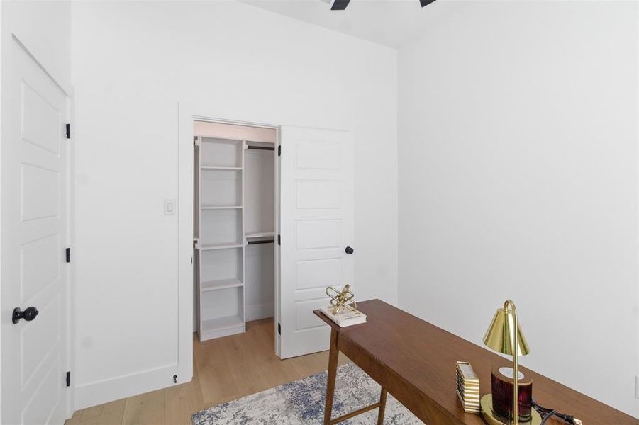 Room featuring wood-finish flooring, white walls, and a built-in closet system with shelving and hanging rods