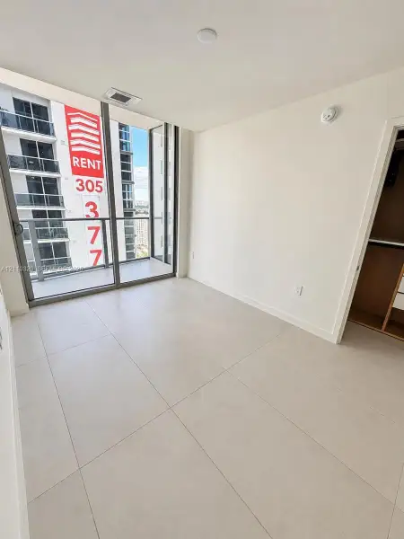 Floor-to-ceiling glass paneling with integrated sliding door access to a private balcony, large-format tile flooring, and a built-in closet system