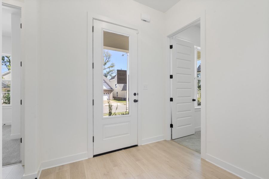 Entryway featuring light-toned wood-finish flooring, a white exterior door with a glass panel, and interior doors with matte black hardware Entryway featuring light-toned wood-finish flooring, a white exterior door with a glass panel, and interior doors with matte black hardware