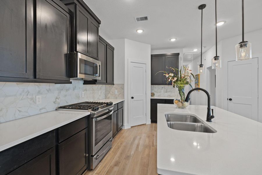 Bright tile and backsplash, double sinks, upgraded stove and cooktop, microwave and pantry in island kitchen.