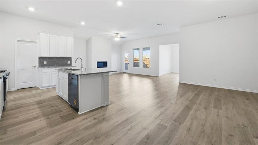 Kitchen featuring open floor plan, a center island with sink, white cabinetry, light stone countertops, and backsplash