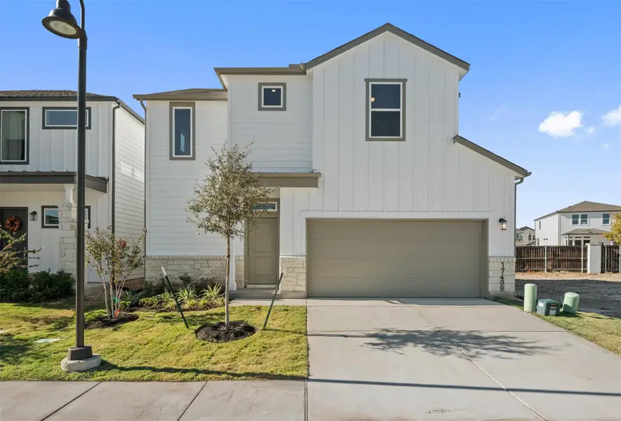 View of front facade featuring board and batten siding, stone siding, concrete driveway, an attached garage, and a front lawn View of front facade featuring board and batten siding, stone siding, concrete driveway, an attached garage, and a front lawn