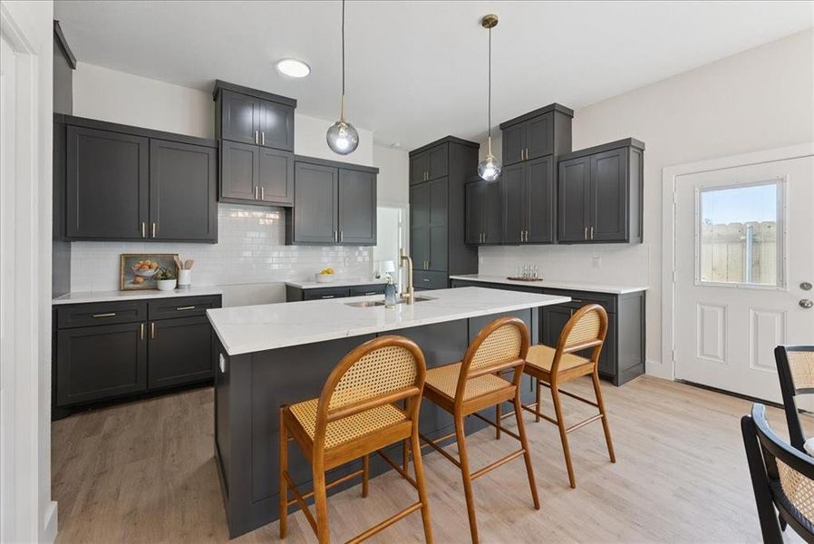 Kitchen featuring backsplash, light stone counters, a breakfast bar, light wood finished floors, and decorative light fixtures