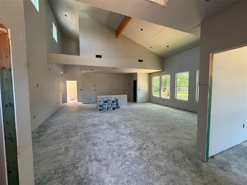Vaulted ceiling with an exposed wood beam, multiple large windows, and a concrete subfloor