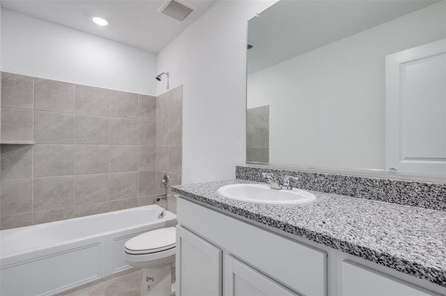 Full bathroom featuring tile flooring, oversized vanity, toilet, and tiled shower / bath combo Full bathroom featuring tile flooring, oversized vanity, toilet, and tiled shower / bath combo