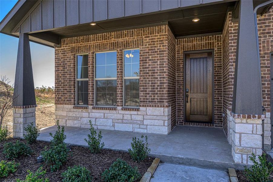 View of exterior entry featuring board and batten siding, covered porch, stone siding, and brick siding