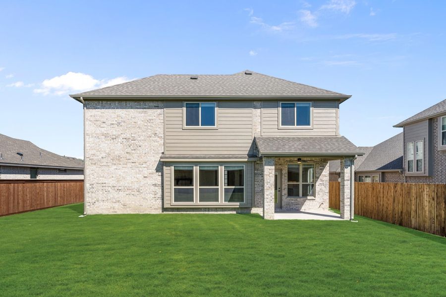 Two-story brick home rear exterior with covered patio, large windows, and fenced backyard lawn