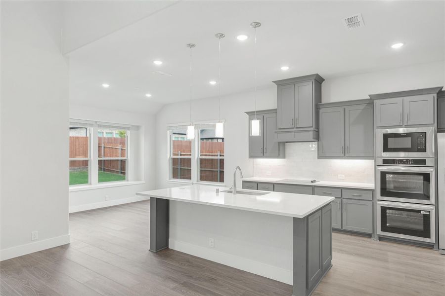 Kitchen with gray cabinets, large center island, white countertops, and stainless steel appliances on wood floors