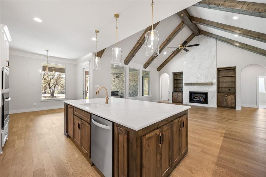 Kitchen featuring open floor plan, a large fireplace, stainless steel appliances, light wood-style flooring, and a kitchen island with sink