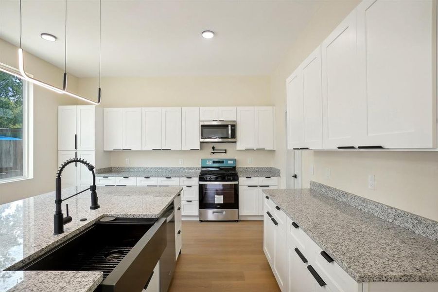 Kitchen with appliances with stainless steel finishes, white cabinetry, light stone countertops, and pendant lighting