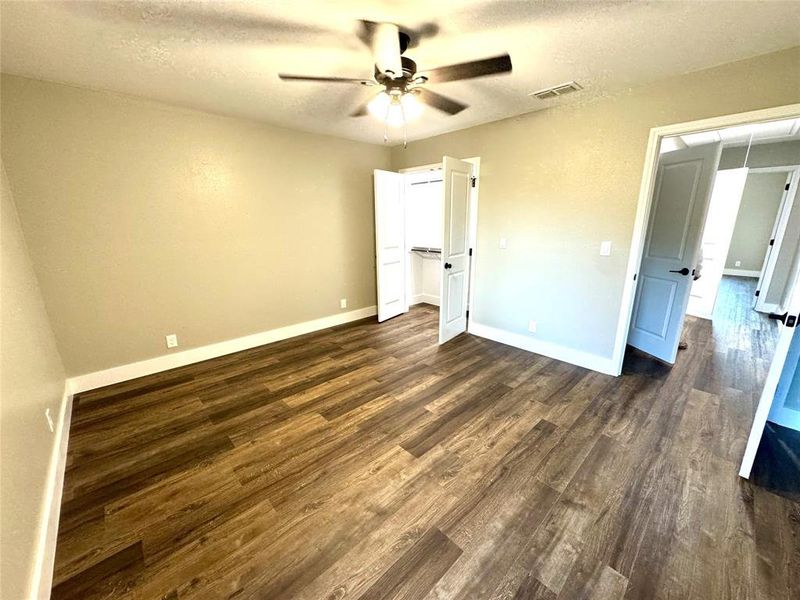 Unfurnished bedroom with a textured ceiling, dark wood-type flooring, ceiling fan, and a spacious closet