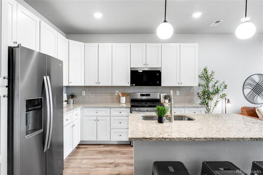 The kitchen features an island, upgraded shaker-style cabinetry, a soft backsplash and neutral granite counters