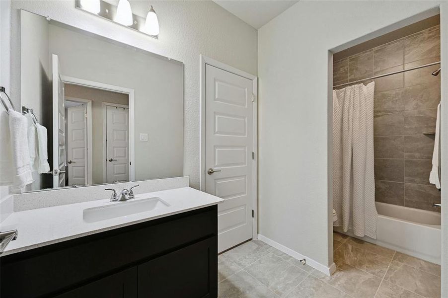 Large secondary full bathroom with quartz countertop and tile flooring.