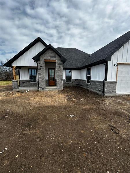 Modern inspired farmhouse with an attached garage, board and batten siding, stone siding, and a shingled roof