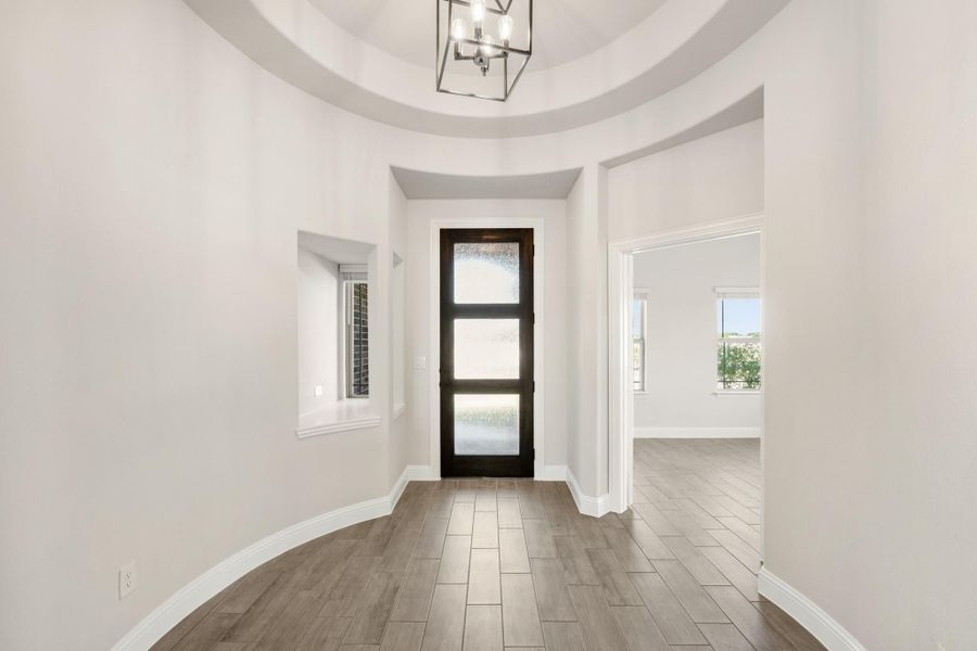 Rounded entryway with dome ceiling, dark wood glass front door, chandelier, and wood-look tile floors Rounded entryway with dome ceiling, dark wood glass front door, chandelier, and wood-look tile floors