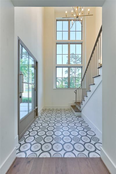 This entryway features a high ceiling with large windows, patterned tile flooring, and a modern chandelier. This entryway features a high ceiling with large windows, patterned tile flooring, and a modern chandelier.
