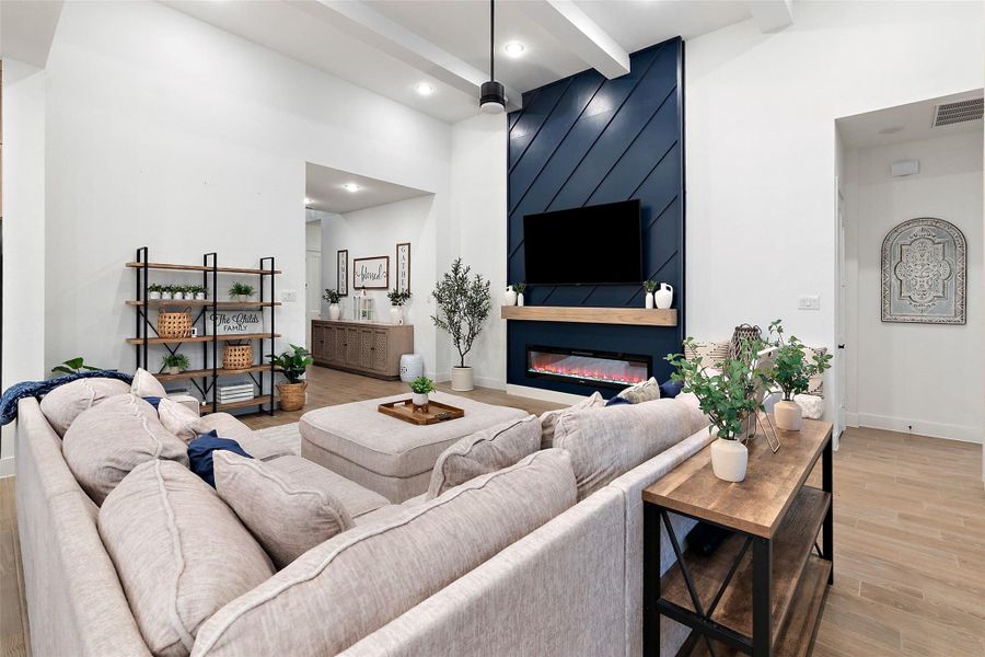 The soaring family room features high ceilings with beams, an electric fireplace wall, and flows into a chef's kitchen with quartz countertops, oversized island, luxe pantry, Barley cabinetry with glass uppers, and GE Profile appliances including double ovens with built-in air fryer. The soaring family room features high ceilings with beams, an electric fireplace wall, and flows into a chef's kitchen with quartz countertops, oversized island, luxe pantry, Barley cabinetry with glass uppers, and GE Profile appliances including double ovens with built-in air fryer.