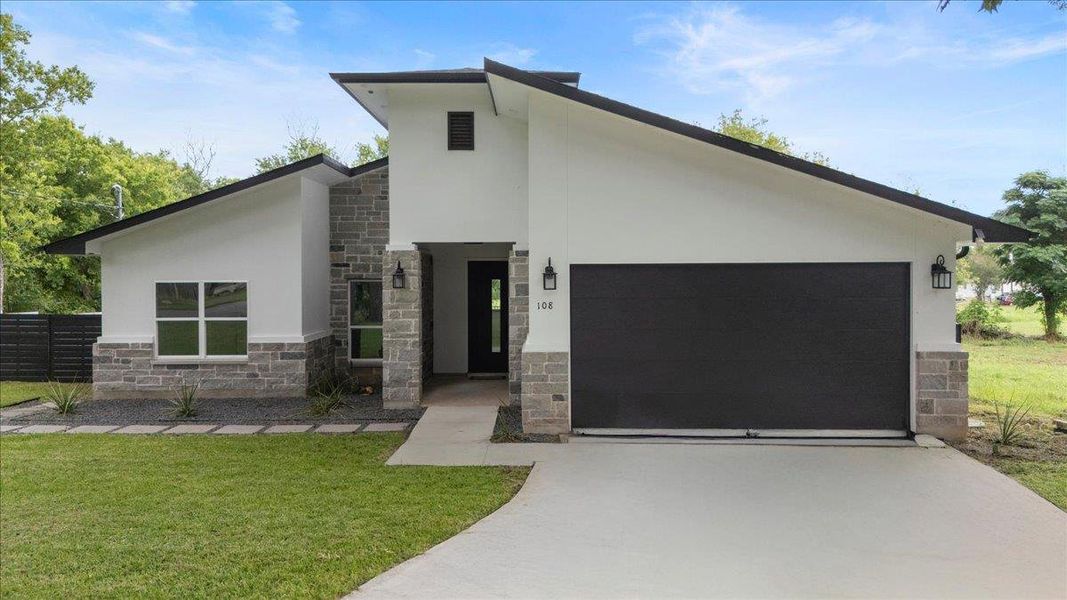 Modern home featuring stone siding, driveway, stucco siding, a garage, and a front yard Modern home featuring stone siding, driveway, stucco siding, a garage, and a front yard