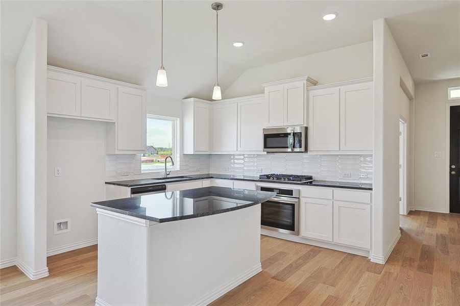 Kitchen with appliances with stainless steel finishes, white cabinetry, light hardwood / wood-style flooring, and tasteful backsplash