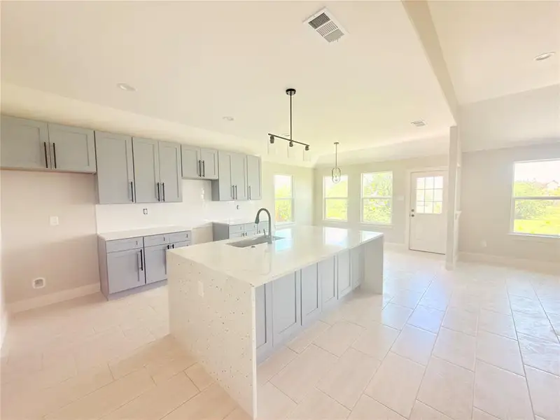 Modern kitchen featuring a spacious center island with a light-colored countertop, light gray cabinetry, and a subway tile backsplash