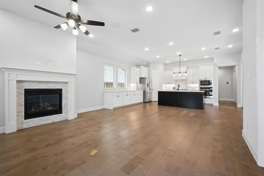 Spacious living area featuring light hardwood flooring, a contemporary fireplace with a stone surround and classic mantel, and a ceiling fan with integrated lighting