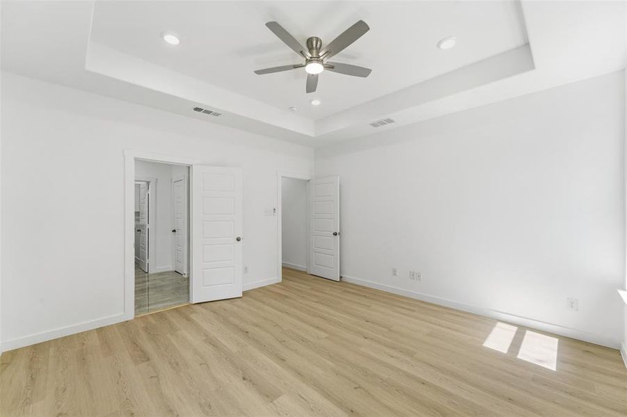 Recessed lighting illuminates a tray ceiling with a brushed nickel ceiling fan