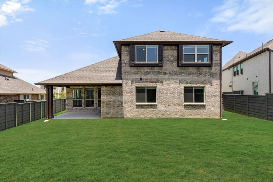 Two-story brick home rear view with covered patio, large green lawn, and dark wood privacy fence Two-story brick home rear view with covered patio, large green lawn, and dark wood privacy fence