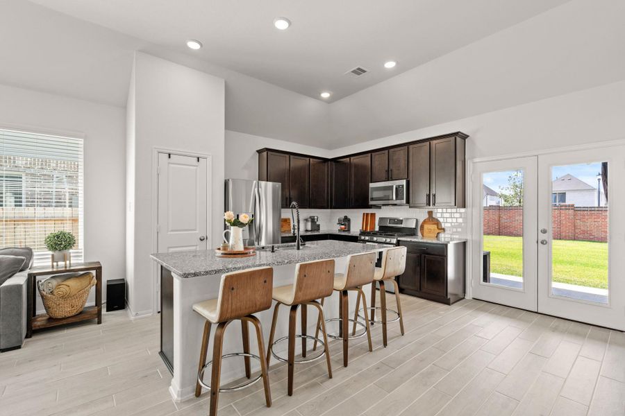 The heart of the home! This  kitchen features elegant cabinetry, a spacious island with seating, sleek stainless steel appliances, and connects directly to the covered patio—perfect for gathering and entertaining.