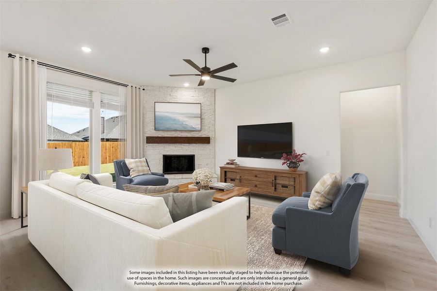 Living room with white brick fireplace, ceiling fan, light wood floors, and white sofa with blue accent chairs Living room with white brick fireplace, ceiling fan, light wood floors, and white sofa with blue accent chairs