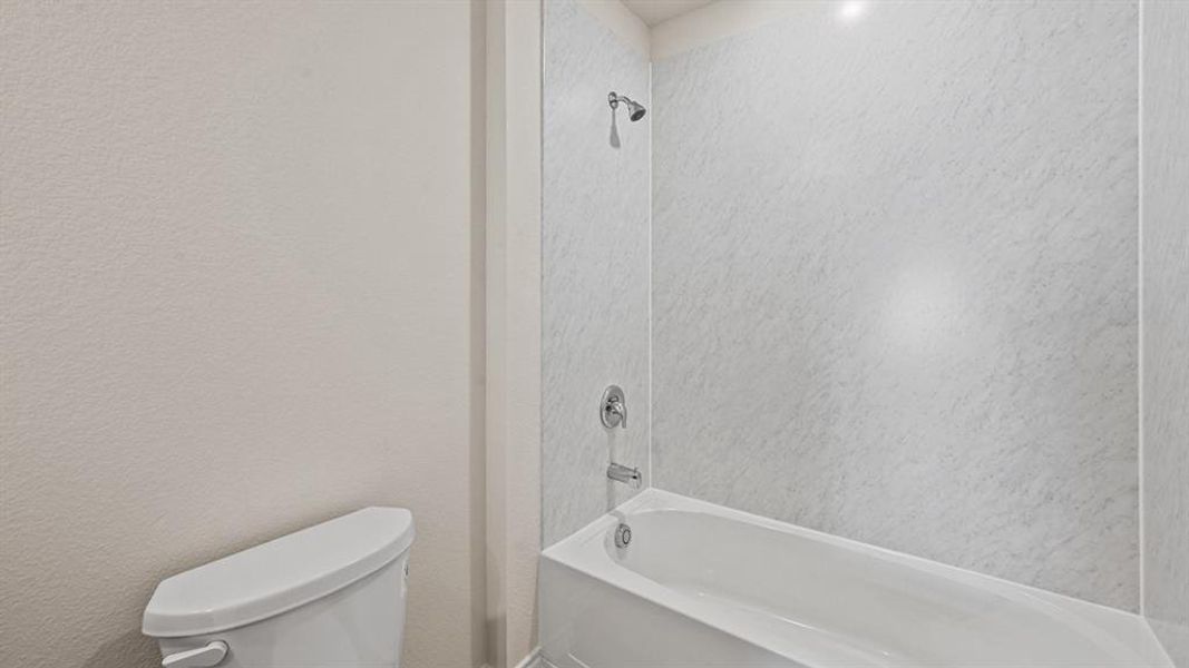 White tub and shower combination with stone-finish surround, chrome fixtures, and overhead lighting