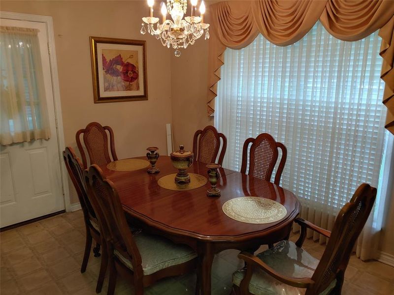 Formal dining space featuring a polished wood-finish table, a crystal chandelier, vertical blinds, and patterned flooring