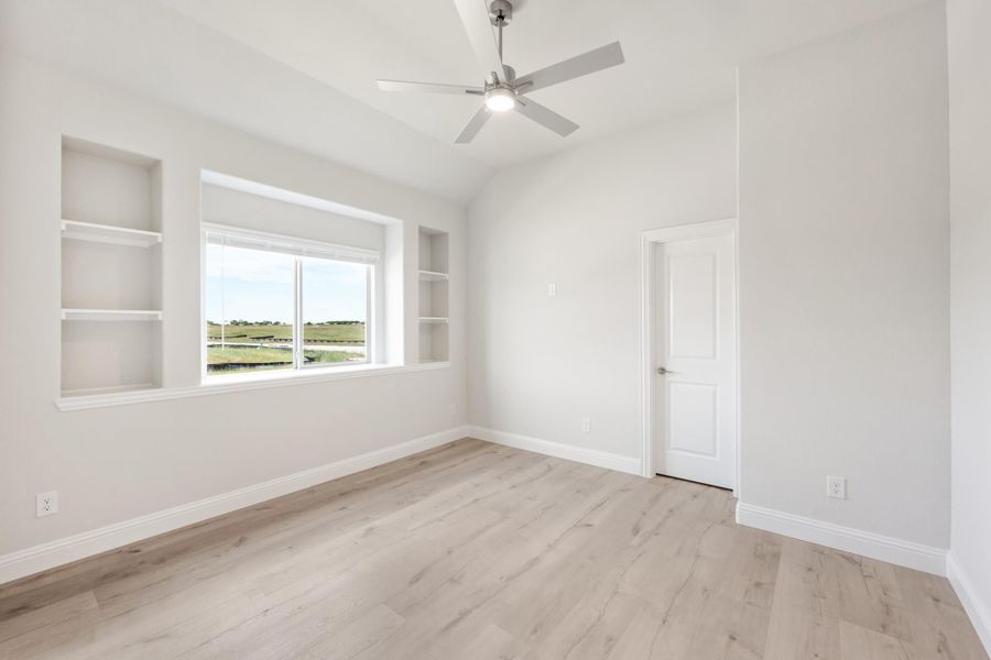 Empty bedroom with vaulted ceiling, ceiling fan, built-in shelves, and light wood floors